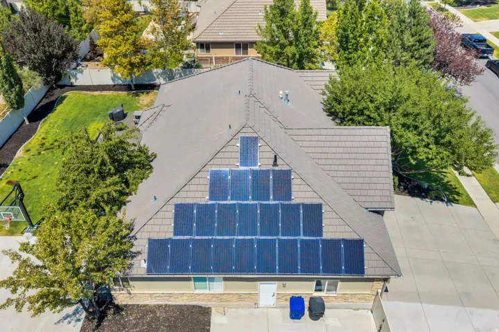 Property featuring a shingle roof with extensive solar panel installation, a stone facade, and a concrete driveway