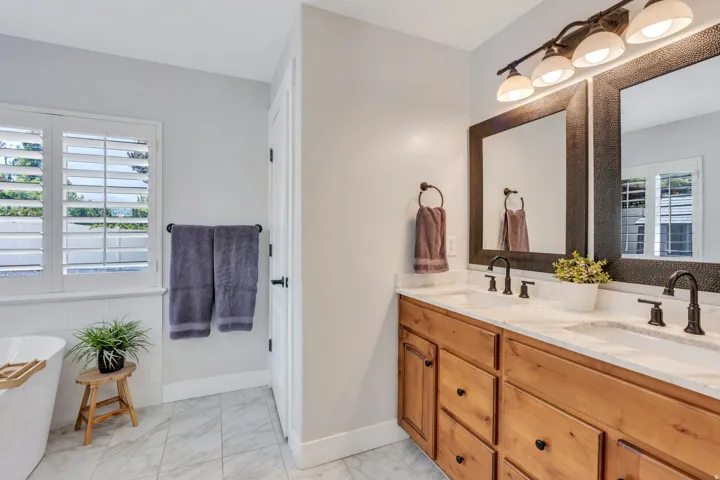 Dual vanity with wood cabinetry, light-toned countertops, and dark bronze fixtures