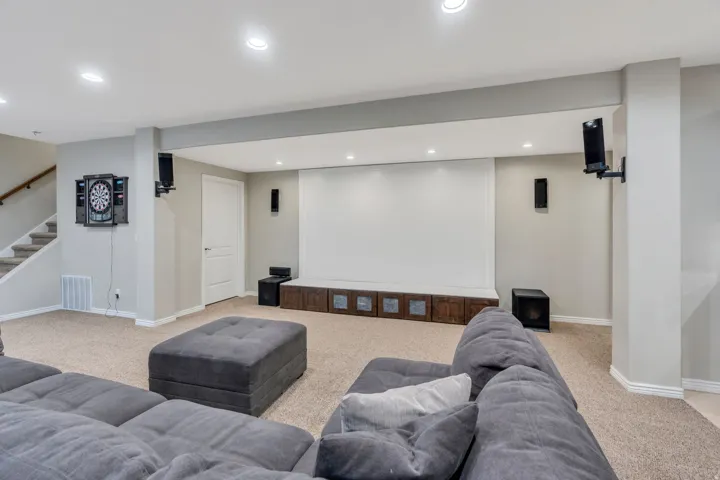 Finished lower level featuring a large projection screen, recessed lighting, carpeted flooring, and a built-in storage console