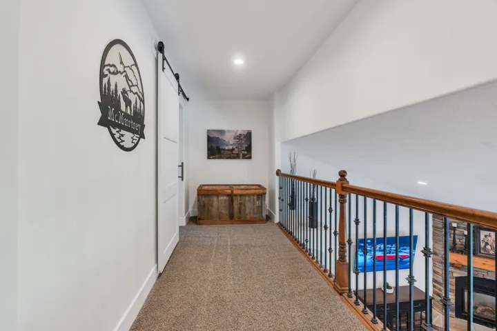 Upper-level hallway featuring a sliding barn door with black hardware, recessed lighting, and light-toned carpet flooring