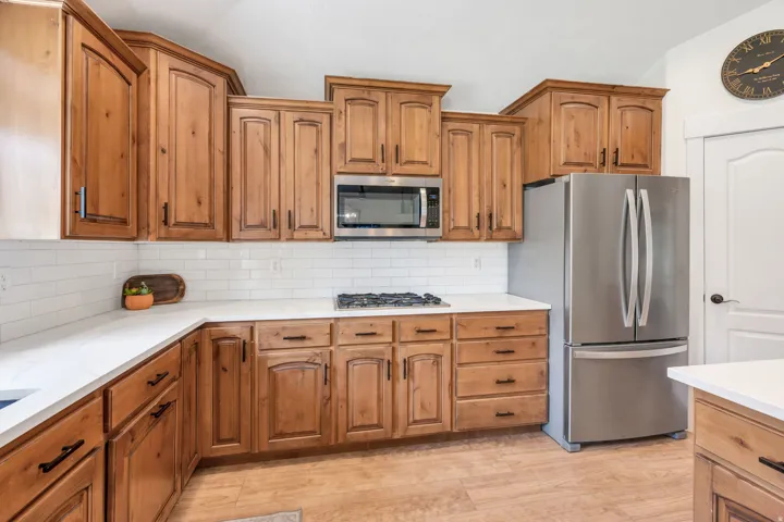 Kitchen featuring wood cabinetry with dark hardware, white countertops, white subway tile backsplash, stainless steel appliances, and wood-finish flooring