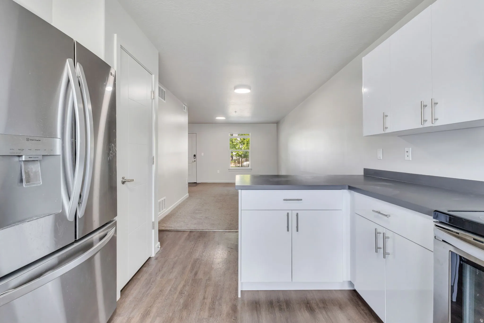 Wood-finish flooring with white cabinetry, a stainless steel refrigerator, and dark countertops