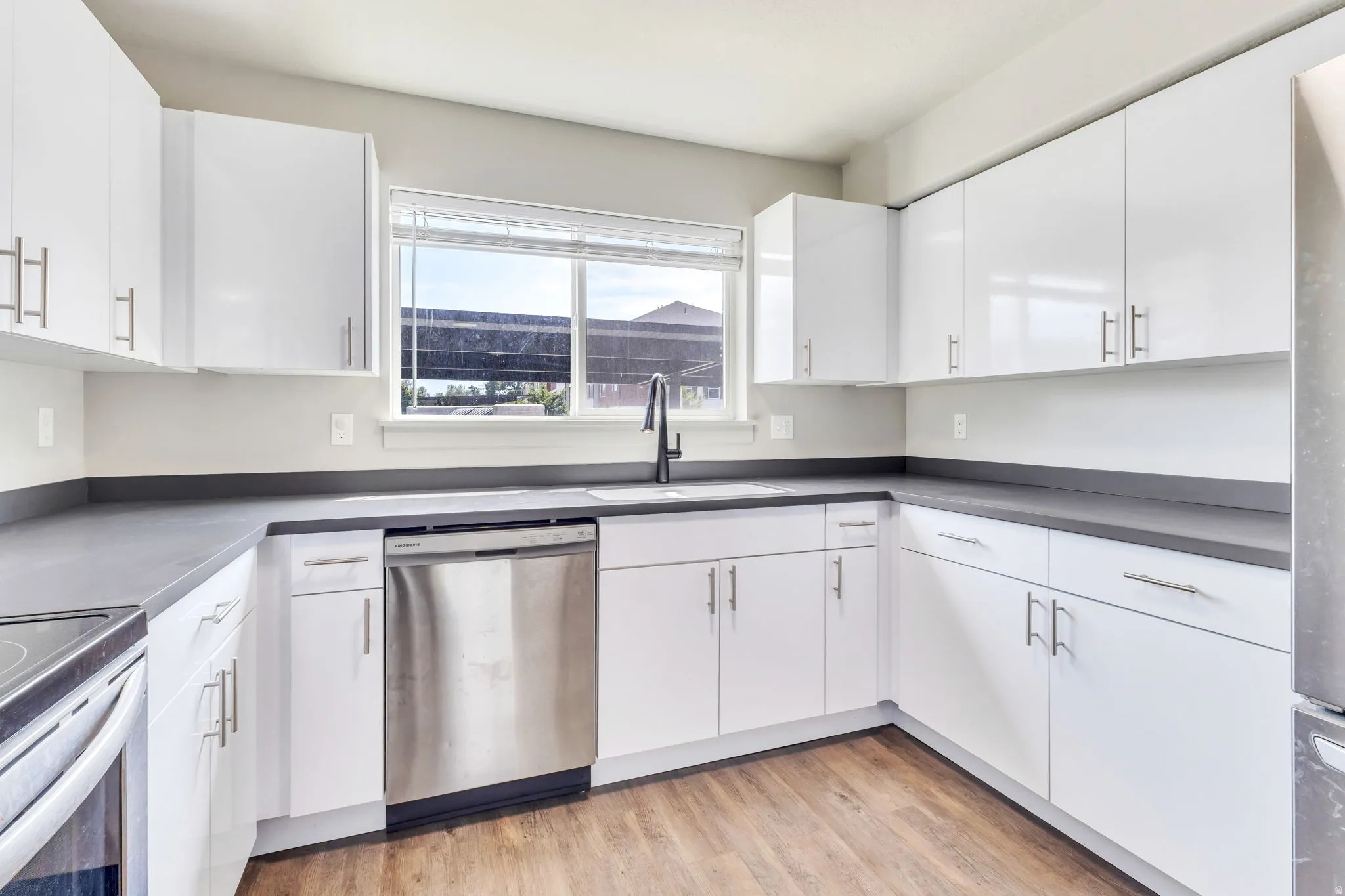 Kitchen featuring white cabinetry, dark countertops, wood-finish flooring, and stainless steel appliances