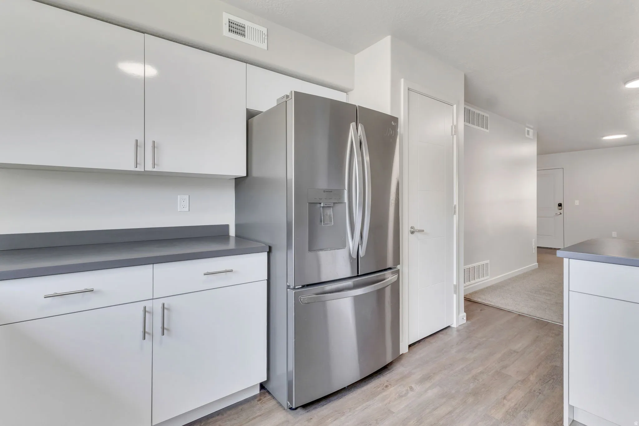 Modern kitchen featuring white cabinetry with stainless steel hardware, a gray quartz countertop, and stainless steel French-door refrigerator with ice and water dispensers