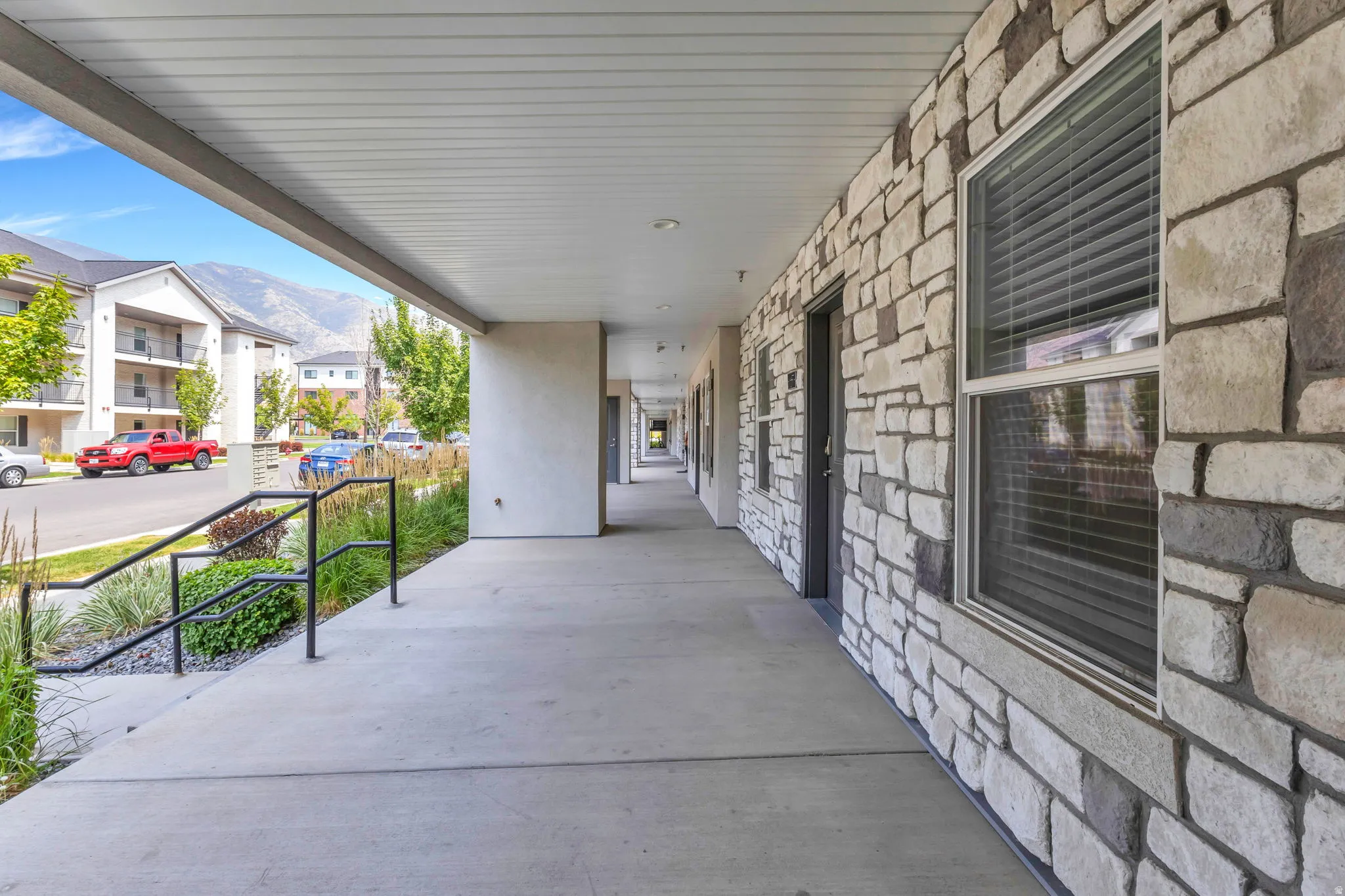 Covered breezeway with concrete flooring and stone veneer exterior, offering a sheltered walkway with metal railing and access to multiple ground-level entries