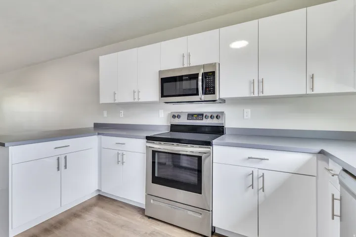 White cabinetry with brushed nickel hardware, stainless steel range, stainless steel microwave, and wood-finish flooring