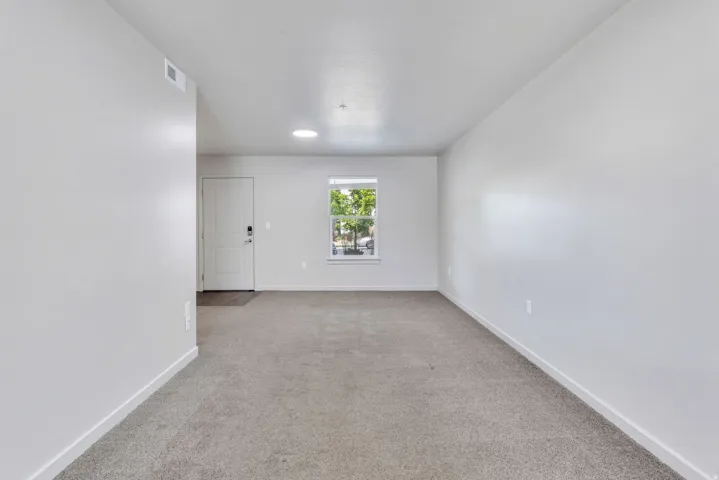 Spacious room featuring neutral carpet flooring, light-colored walls, a single window, a white interior door, and a flush-mount ceiling light fixture