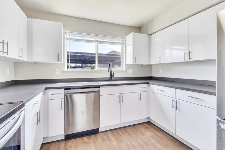 Kitchen featuring white cabinetry, dark countertops, wood-finish flooring, and stainless steel appliances