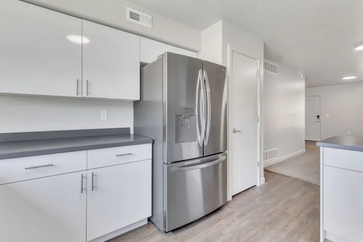 Modern kitchen featuring white cabinetry with stainless steel hardware, a gray quartz countertop, and stainless steel French-door refrigerator with ice and water dispensers