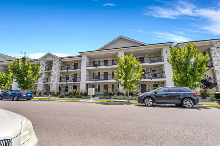 Multi-story building featuring stone veneer accents, multiple balconies with black railings, and landscaping with mature trees