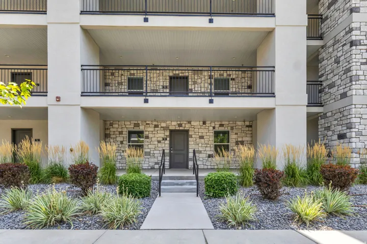 Multi-story exterior with stone-finish siding, black metal railings, and a concrete walkway