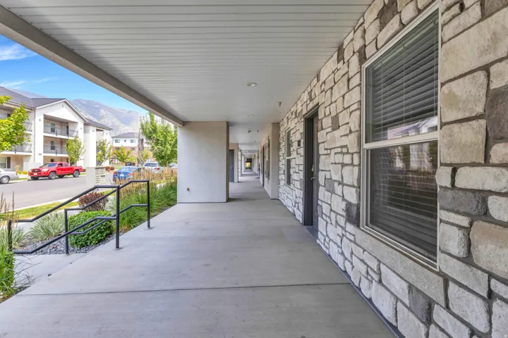 Covered breezeway with concrete flooring and stone veneer exterior, offering a sheltered walkway with metal railing and access to multiple ground-level entries