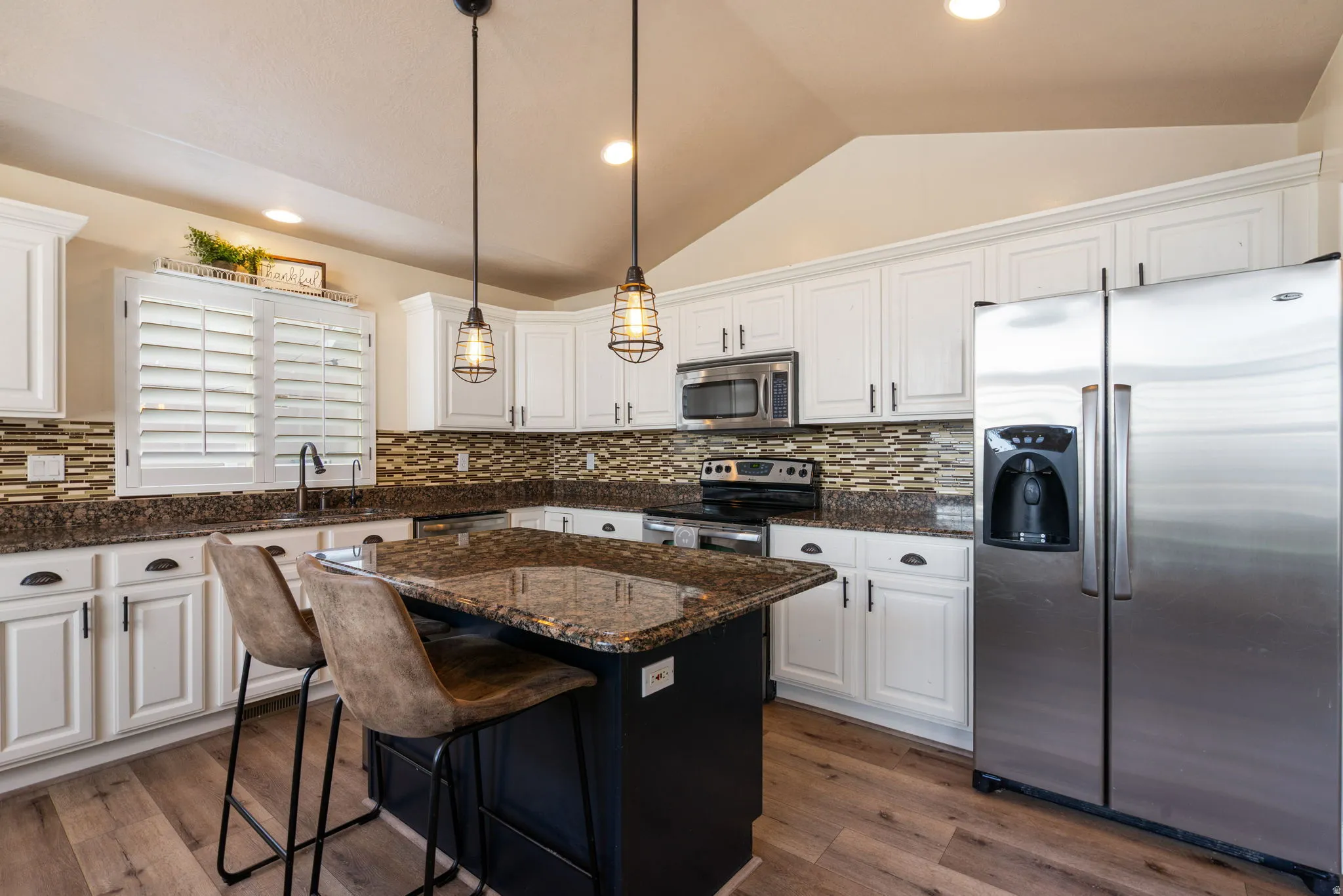 White cabinetry, stainless steel appliances, mosaic tile backsplash, wood-finish flooring, and a central island with a stone countertop