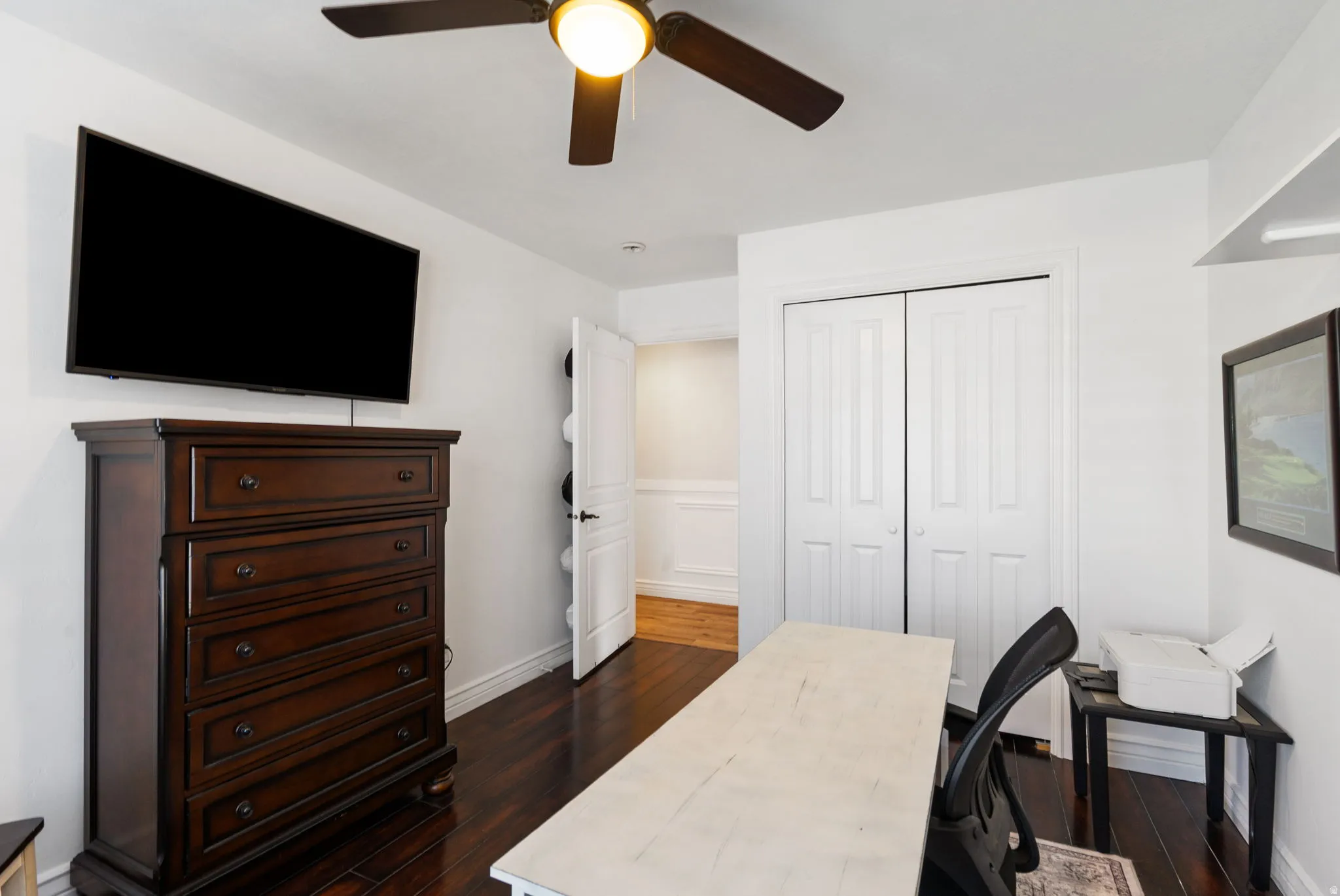 Dark wood-finish flooring, ceiling fan with integrated lighting, and white bi-fold closet doors