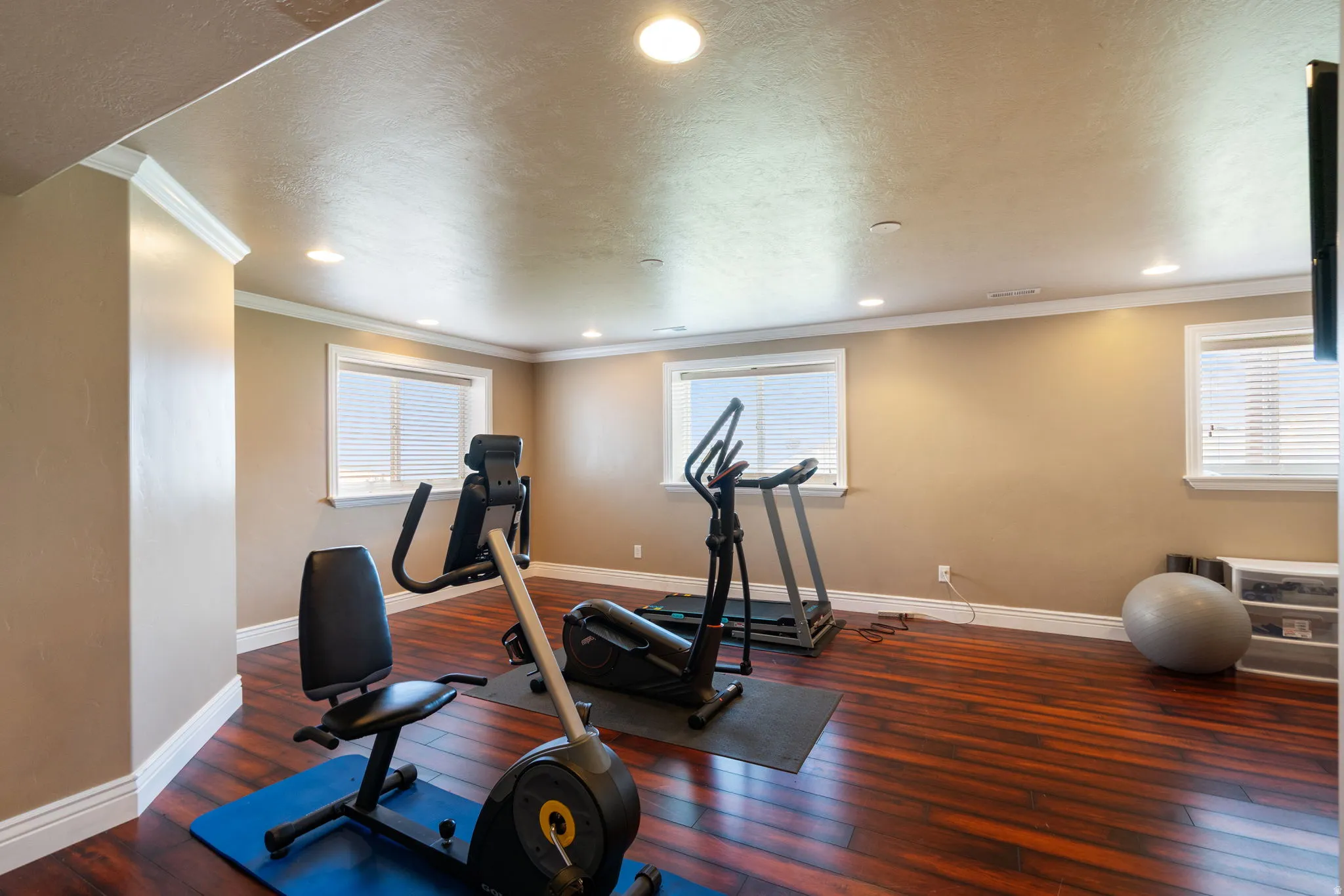 Dedicated fitness room featuring wood-finish flooring, recessed ceiling lighting, and multiple windows providing natural light