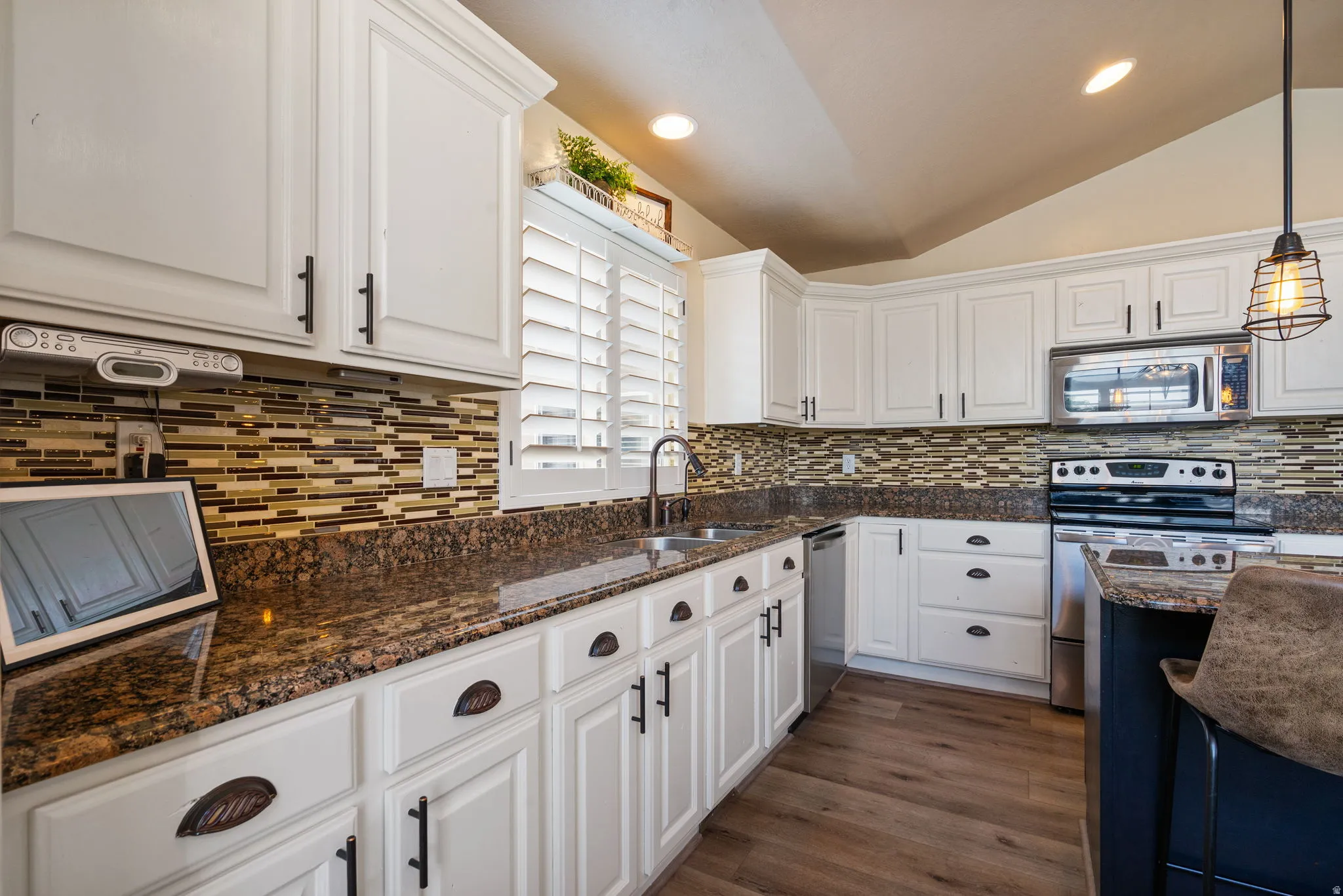 Chef's kitchen featuring white cabinetry with oil-rubbed bronze hardware, granite countertops, mosaic tile backsplash, stainless steel appliances including double wall ovens, and warm wood-finish flooring throughout