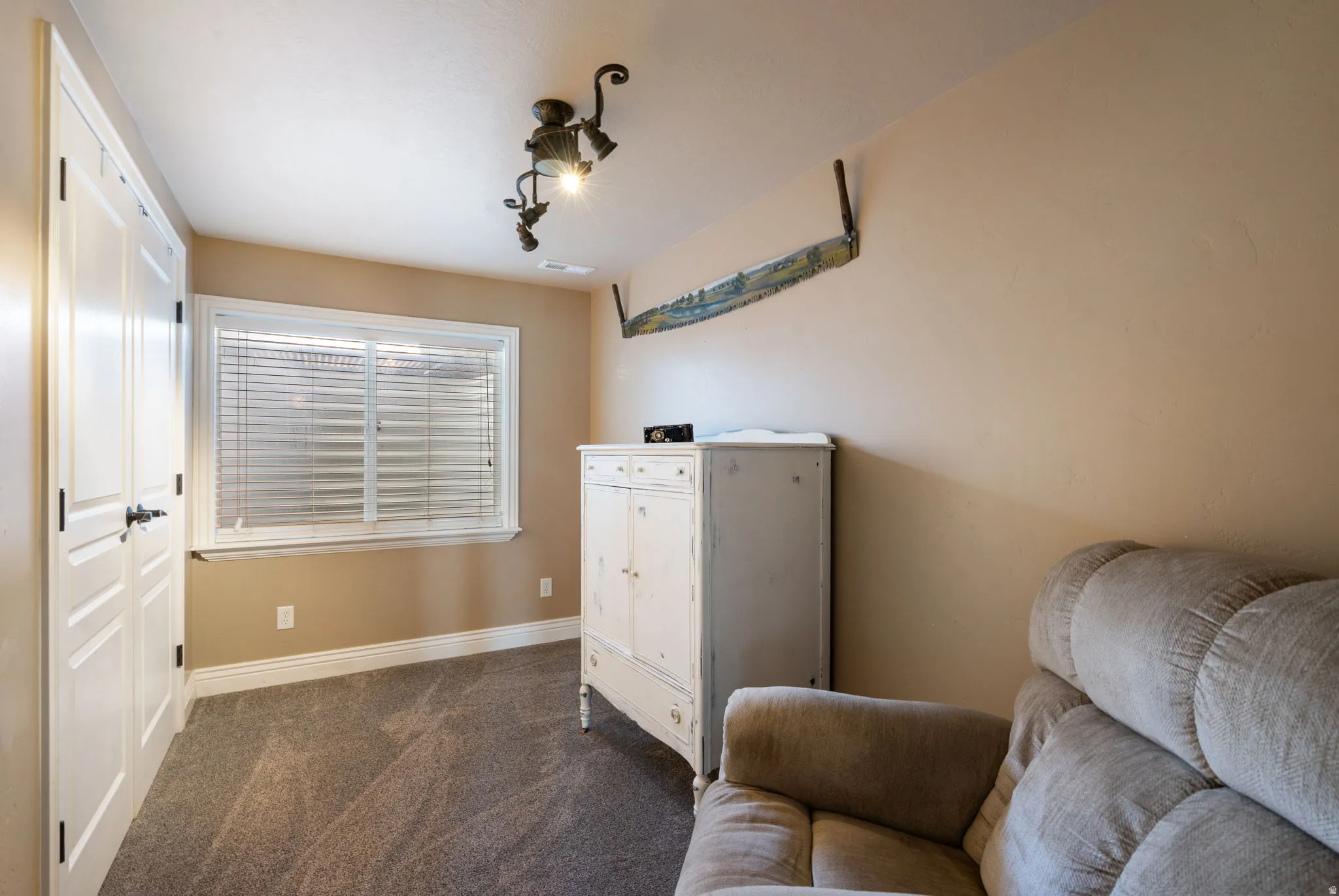 Versatile bedroom space featuring neutral wall finishes, carpeted flooring, a large window with plantation shutters providing natural light, and built-in storage cabinetry