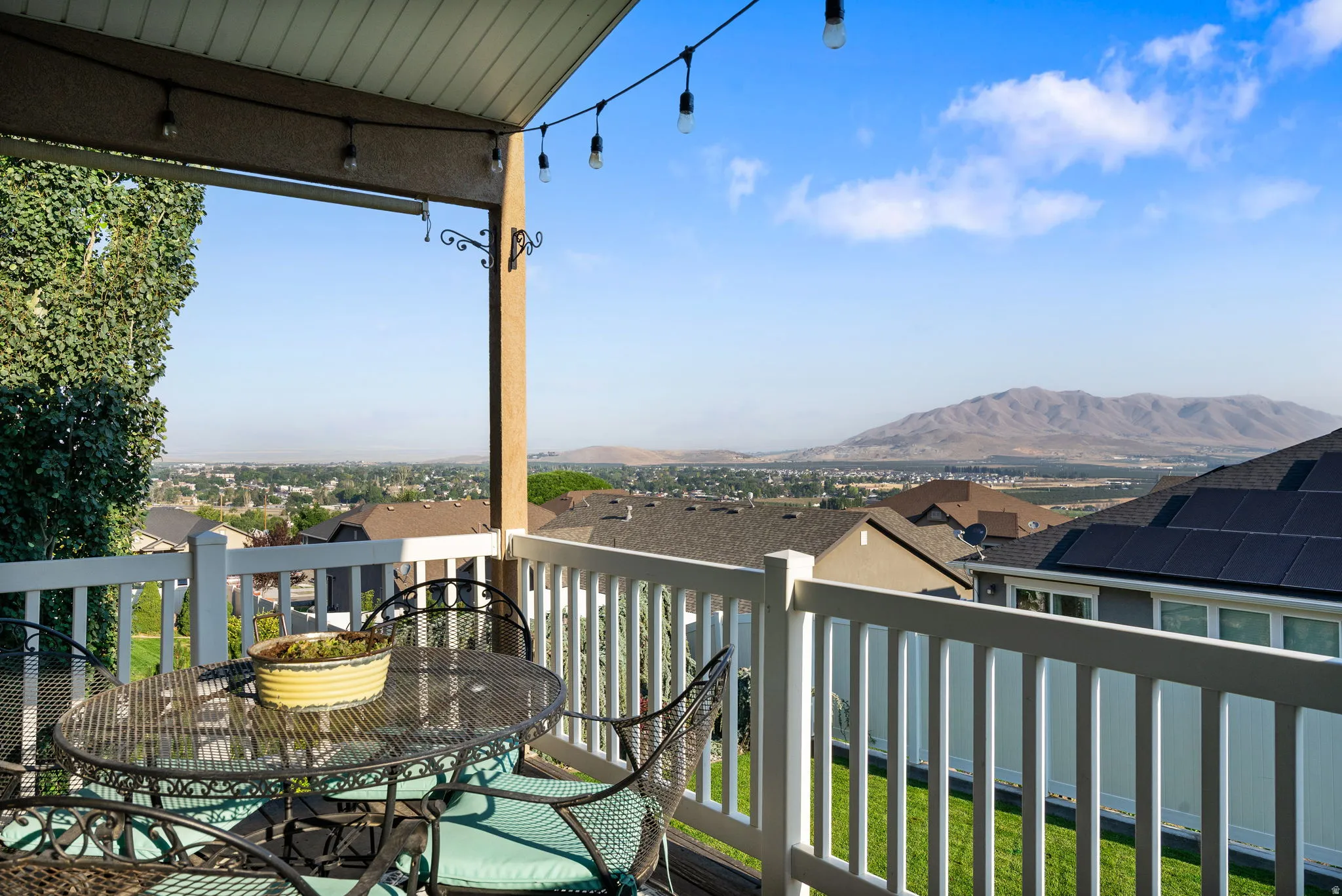Elevated deck with white composite railing and overhead pergola structure, featuring pendant lighting and access to expansive panoramic vistas of manicured grounds, distant mountain ranges, and surrounding valley landscape