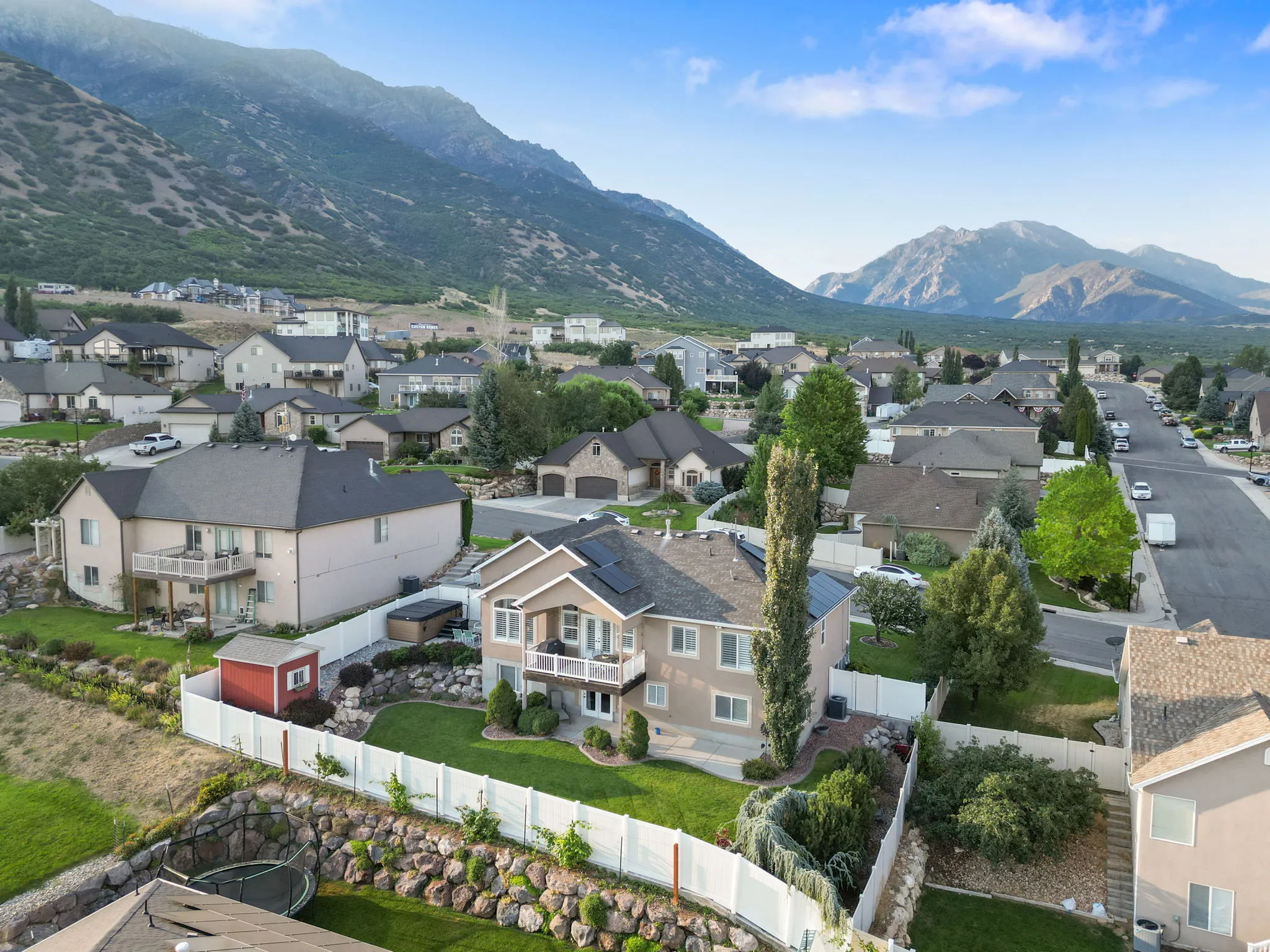 Expansive backyard featuring a manicured lawn, white privacy fence, and rock retaining wall