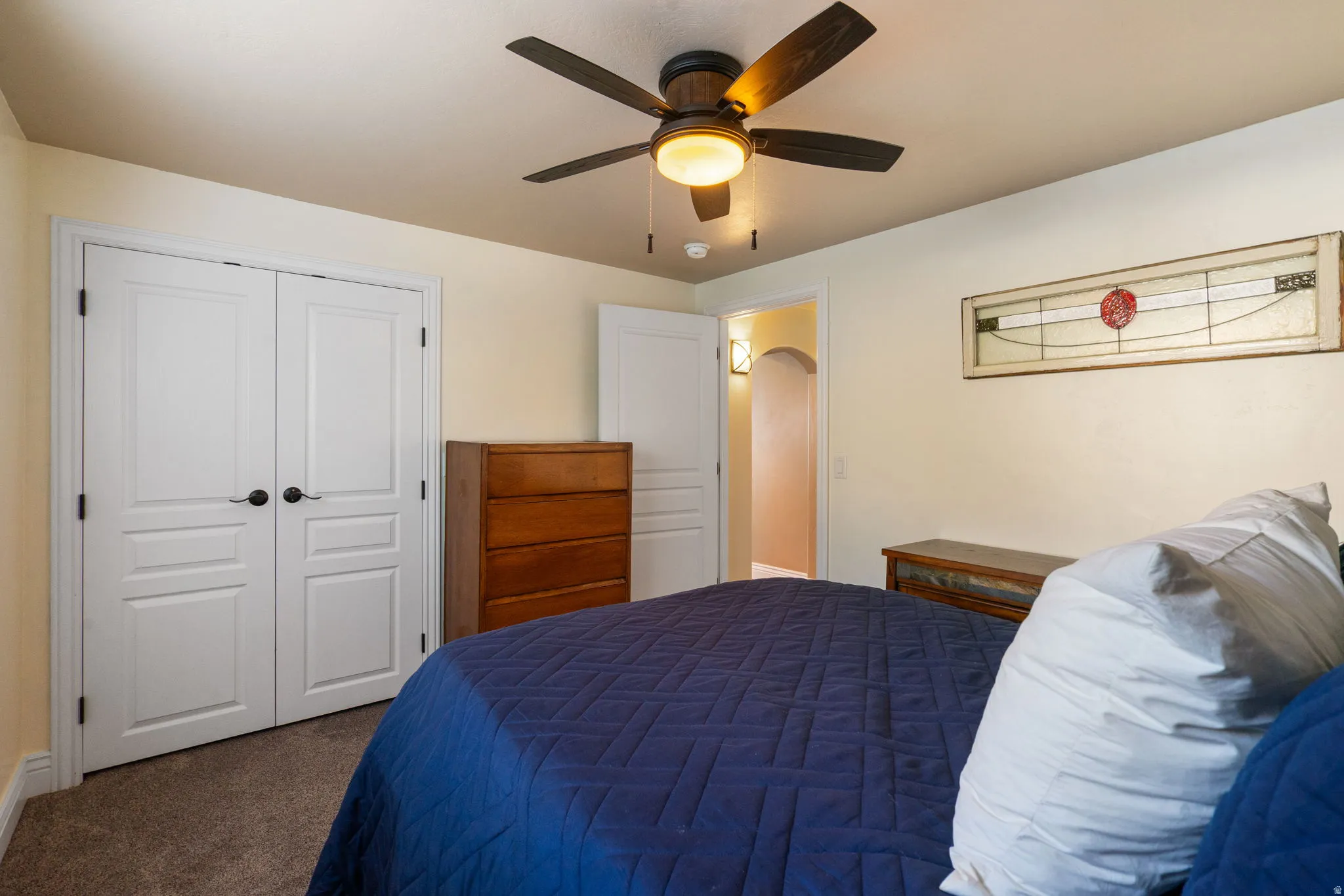 Carpeted room with a ceiling fan, white paneled doors, and an arched doorway
