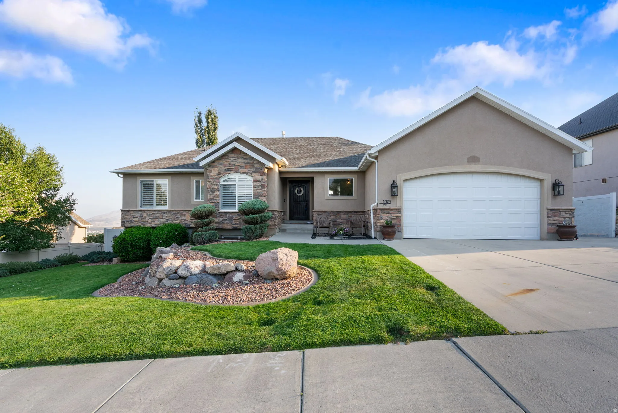 Stucco exterior with stone accents, a landscaped front yard, concrete driveway, and attached garage