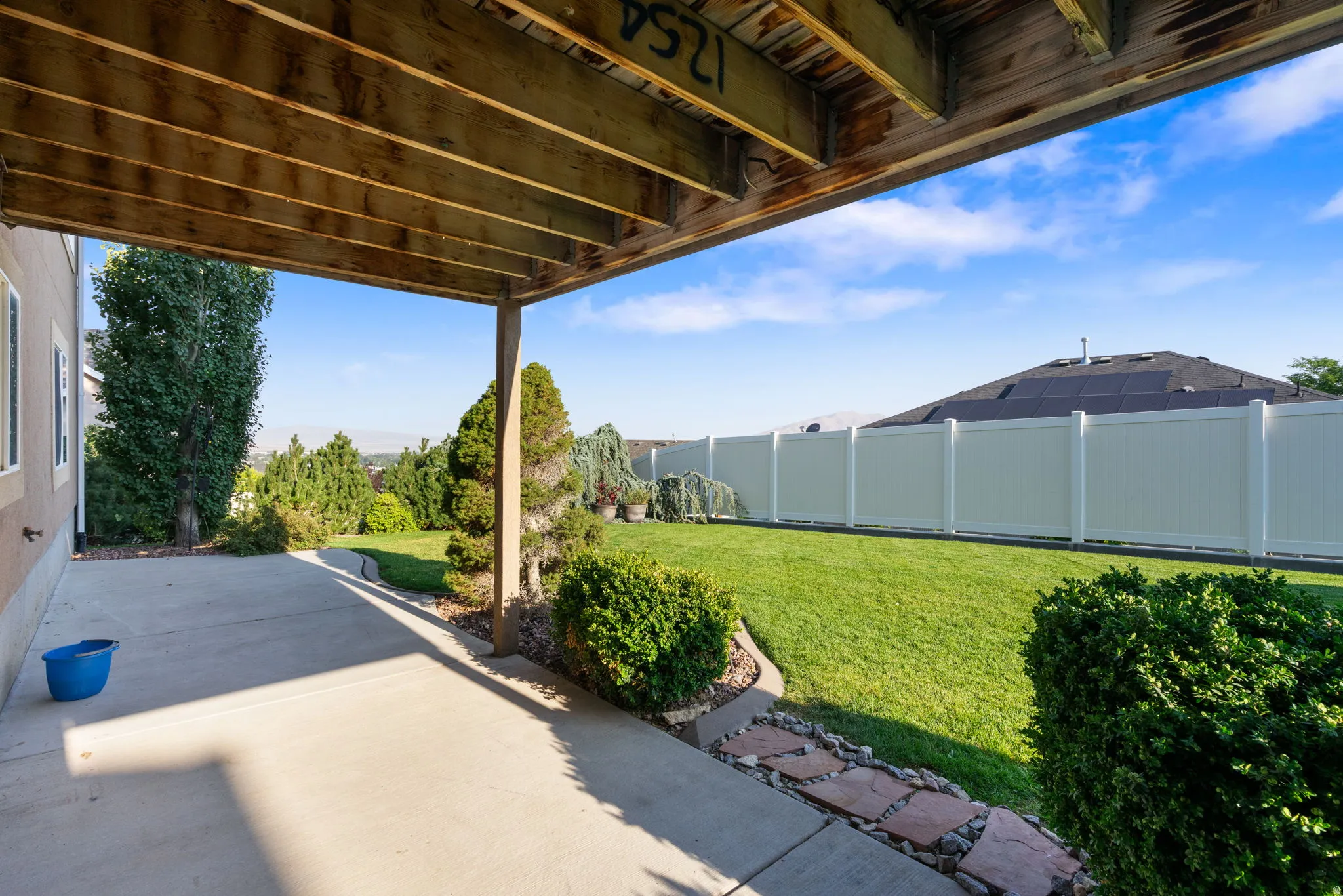Expansive backyard oasis featuring a composite deck with overhead pergola, manicured lawn, mature landscaping with boxwood hedging, and vinyl privacy fencing