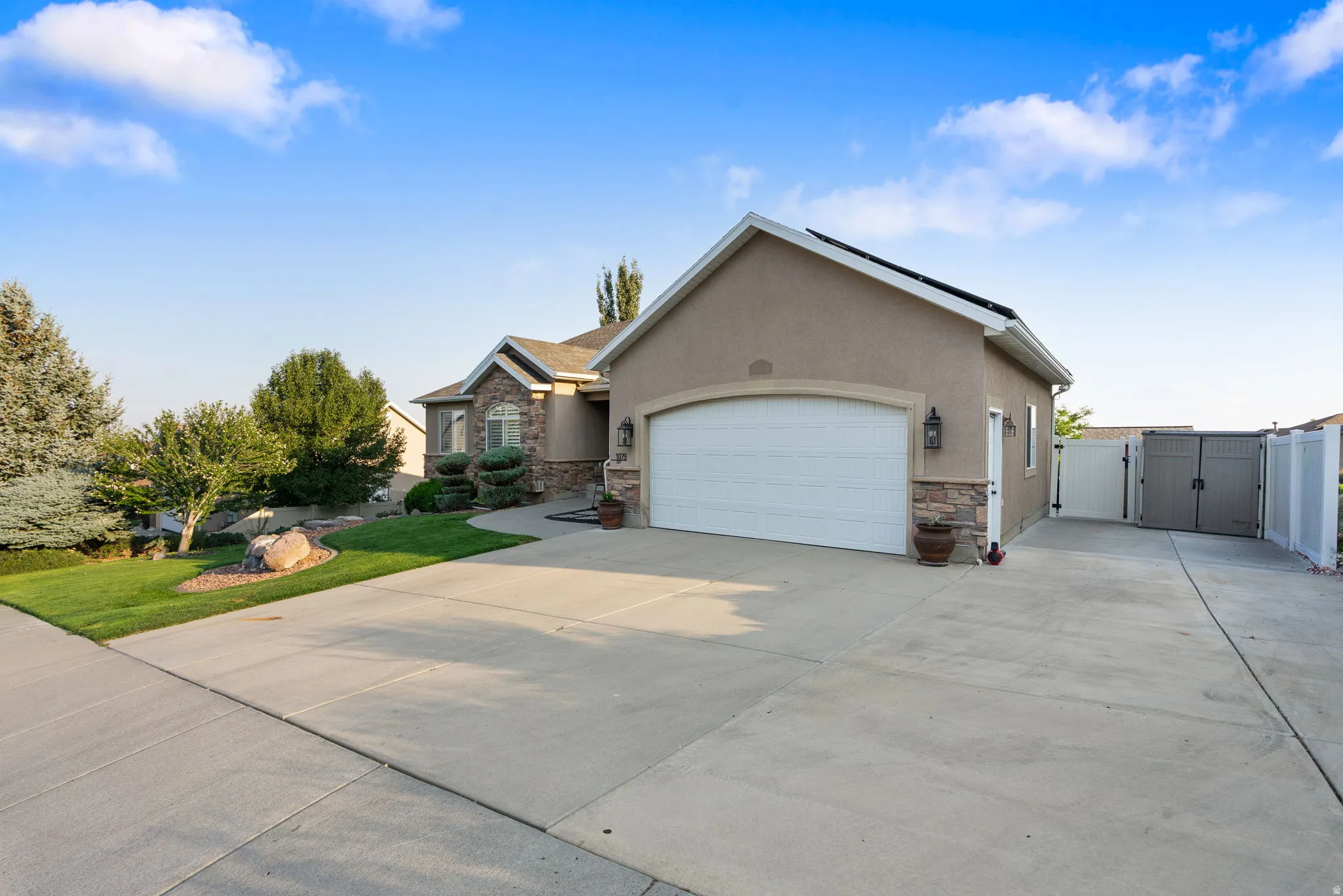 Two-car garage with an arched door, stone veneer detailing, stucco exterior, concrete driveway, and side yard access with gates