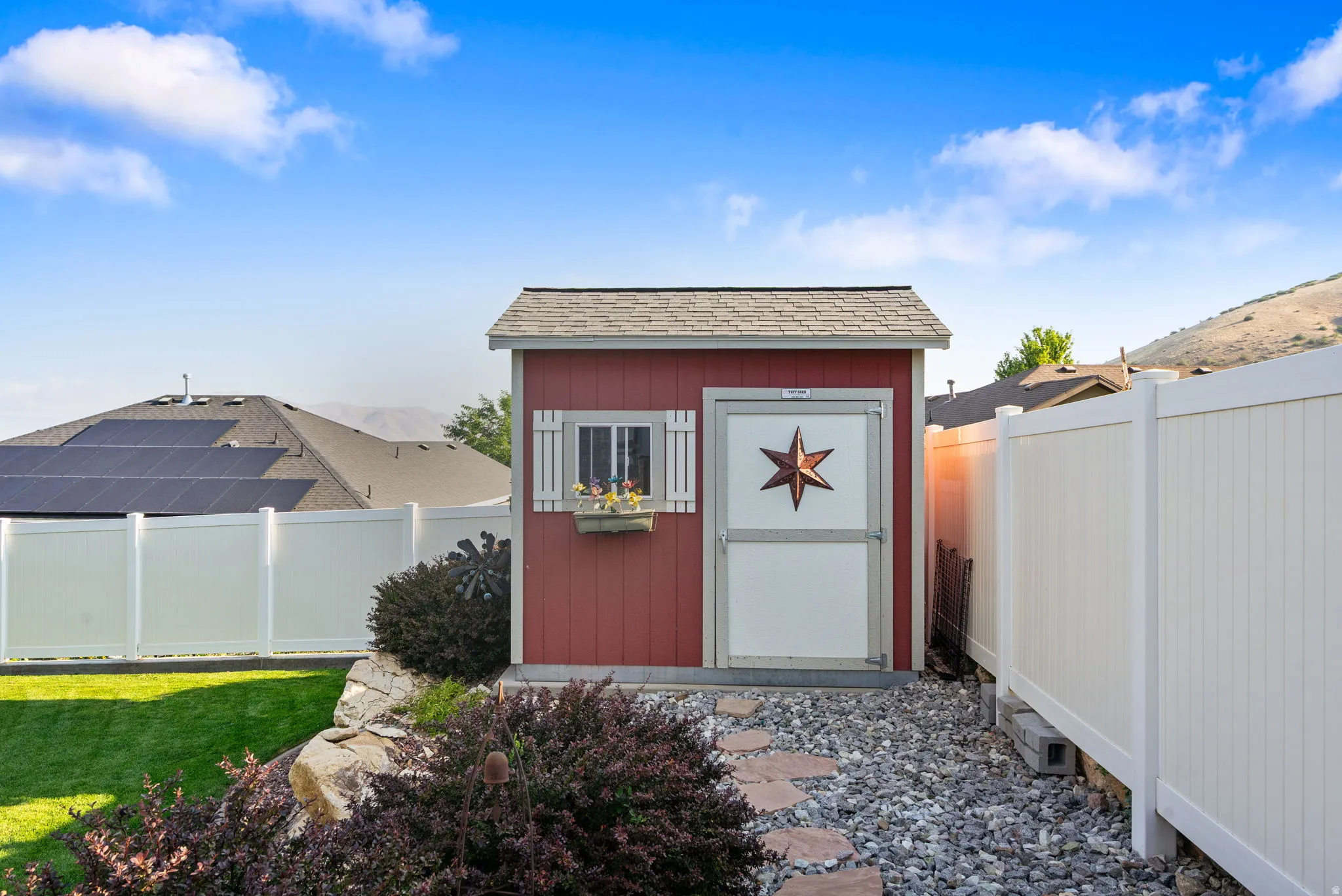 Charming backyard retreat featuring a custom shed with red board-and-batten siding, decorative star accent, and shingled roof