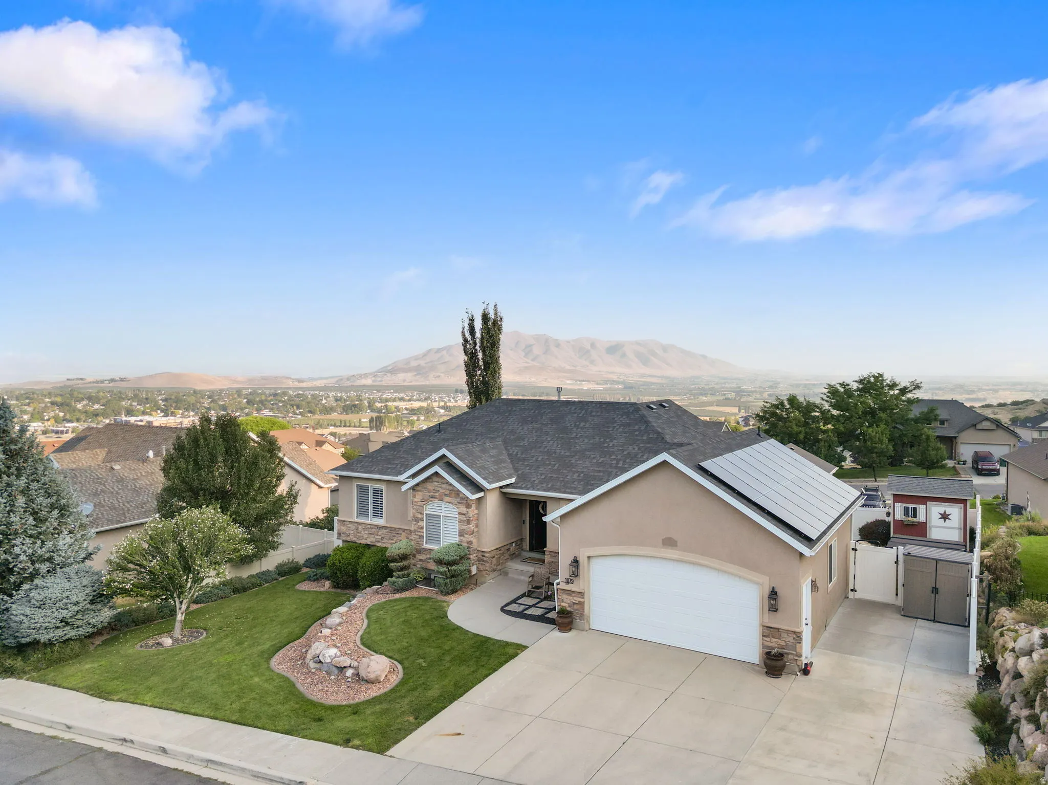 Stucco and stone exterior with an attached garage, featuring a concrete driveway and solar panels