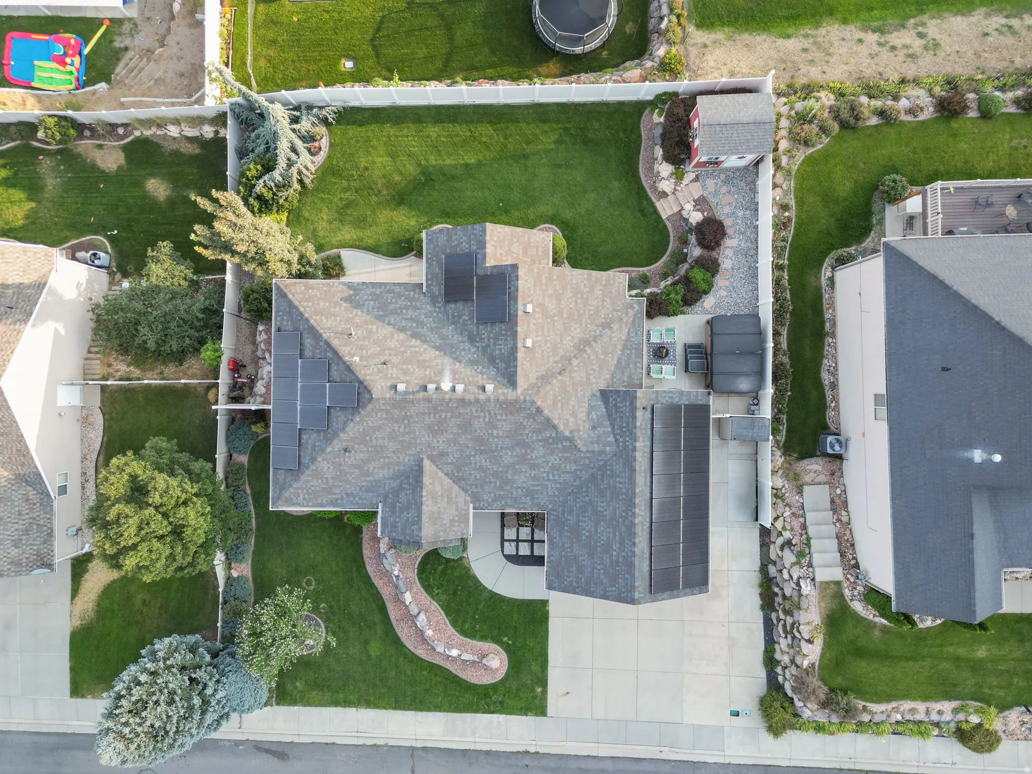 Pitched roofline with solar panels, mature landscaping, manicured lawn, stone pathway, and a detached shed