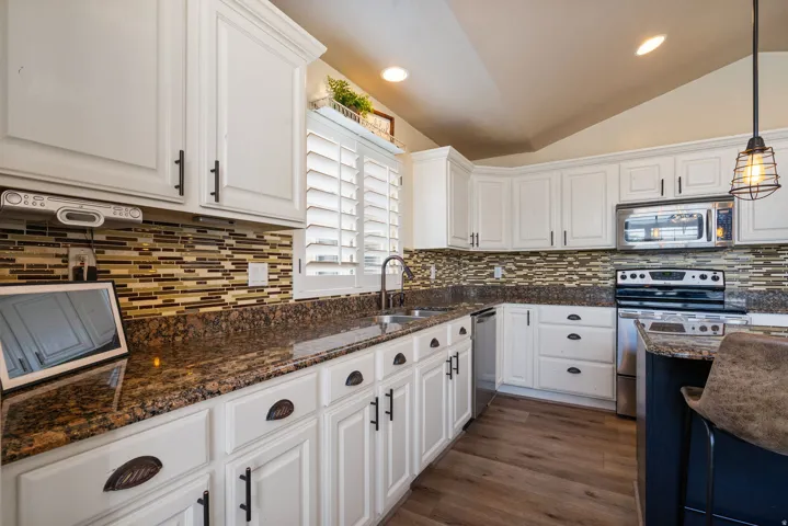 Chef's kitchen featuring white cabinetry with oil-rubbed bronze hardware, granite countertops, mosaic tile backsplash, stainless steel appliances including double wall ovens, and warm wood-finish flooring throughout