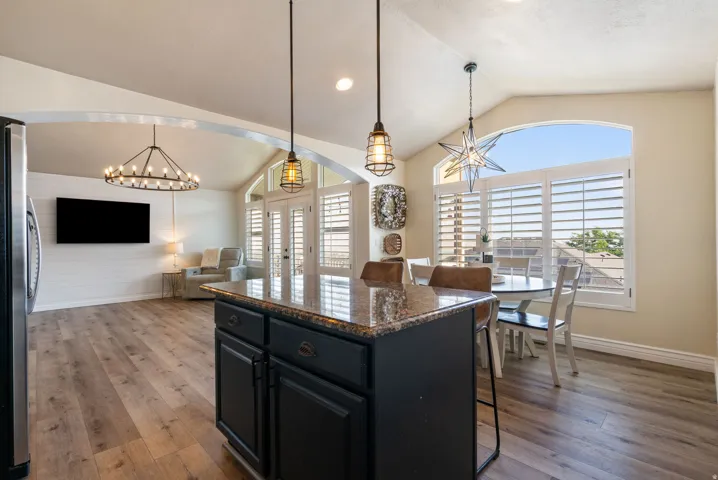 Kitchen island with a stone countertop, vaulted ceilings, wood-finish flooring, white shiplap accent wall, and arch-top windows
