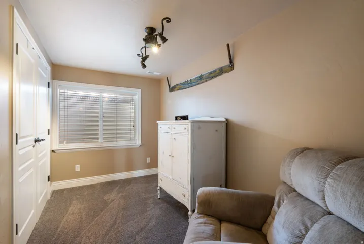 Versatile bedroom space featuring neutral wall finishes, carpeted flooring, a large window with plantation shutters providing natural light, and built-in storage cabinetry