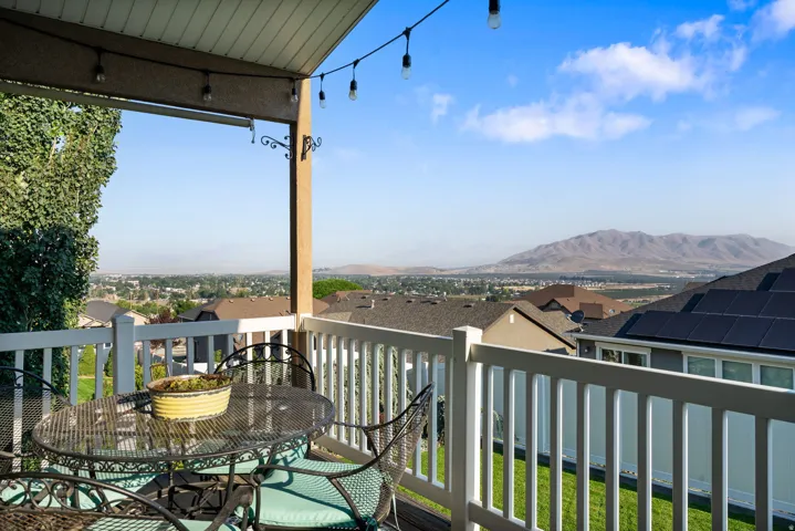 Elevated deck with white composite railing and overhead pergola structure, featuring pendant lighting and access to expansive panoramic vistas of manicured grounds, distant mountain ranges, and surrounding valley landscape