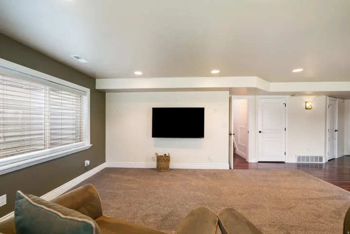 Spacious recreation room with recessed ceiling lighting, large flat-screen-ready wall mount, wood-finish flooring, and abundant natural light from multi-pane windows with plantation shutters