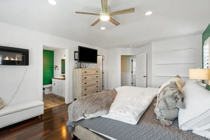 Dark wood-finish flooring, wall-mounted electric fireplace, ceiling fan with integrated lighting, recessed lighting, and built-in shelving