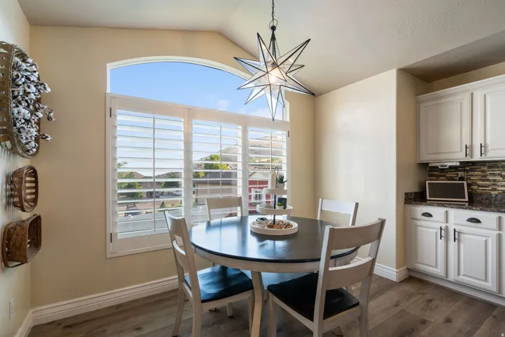 Arched window with plantation shutters, wood-finish flooring, white cabinetry, dark countertop, and decorative tile backsplash