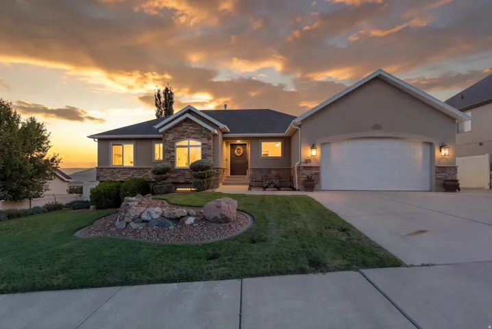 Stucco exterior with stone accents, attached garage, concrete driveway, front lawn, and landscaped rock feature