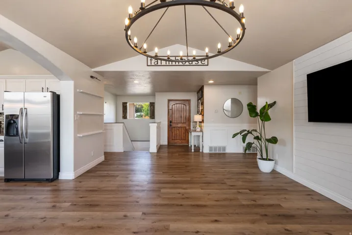 Open-concept living area showcasing hardwood flooring, stainless steel refrigerator, white cabinetry, and a modern circular pendant light fixture suspended from a vaulted ceiling