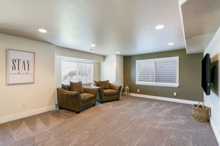 Recessed ceiling lighting, two windows with blinds, wall-mounted television bracket, neutral carpeting, and contrasting paint palette