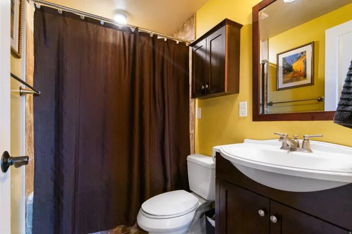 Bright and updated bathroom featuring vibrant yellow walls, dark wood cabinetry with dual-sink vanity, curved ceramic sink basin, chrome faucet fixtures, and a separate toilet
