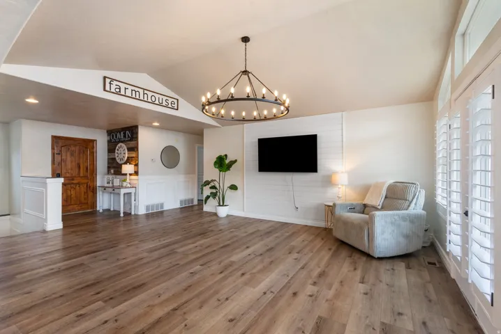 Spacious open-concept living area featuring hardwood flooring throughout, a statement chandelier with Edison-style bulbs, and a wall-mounted flat-screen television