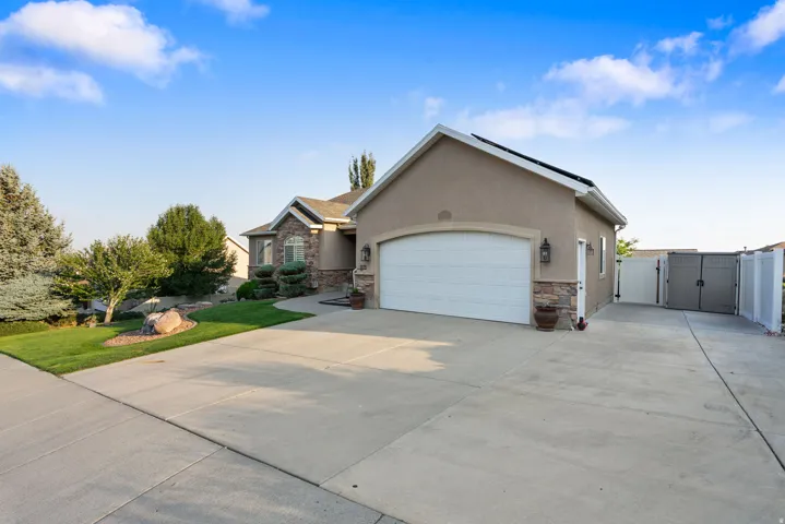 Two-car garage with an arched door, stone veneer detailing, stucco exterior, concrete driveway, and side yard access with gates