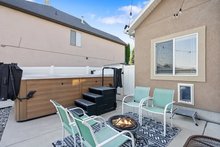 Concrete patio with a built-in spa featuring wood-finish paneling, a fire pit, and string lighting