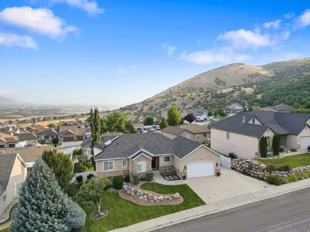 Stunning hilltop residence featuring a clean-lined stucco exterior with a dark asphalt shingle roof, circular driveway, and manicured landscaping with mature trees and ornamental plantings