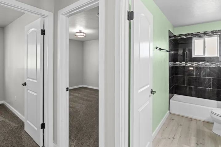 Bathroom featuring a bathtub, dark tile surround with decorative accent, light green walls, and light wood-finish flooring