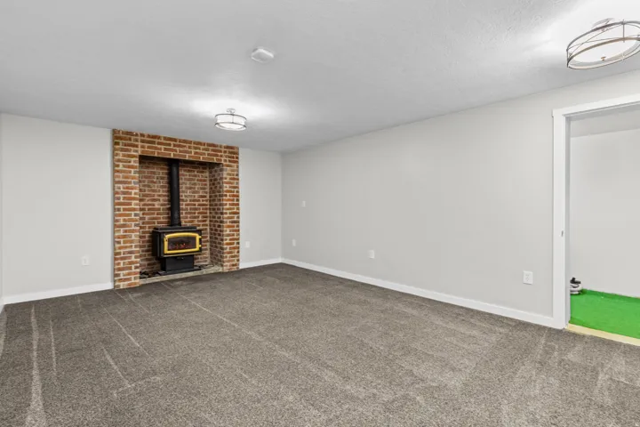 Spacious finished basement featuring neutral carpet flooring, recessed ceiling lighting, and a striking exposed brick fireplace with black metal stove insert