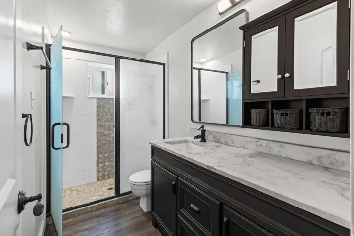 Dark wood-finish flooring with a white tiled shower featuring a mosaic accent