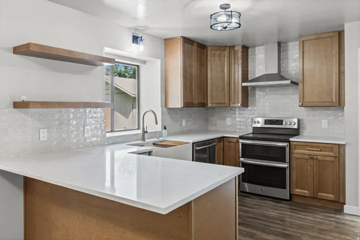 Kitchen featuring light wood-finish cabinetry, white countertops, tile backsplash, stainless steel appliances, and wood-finish flooring