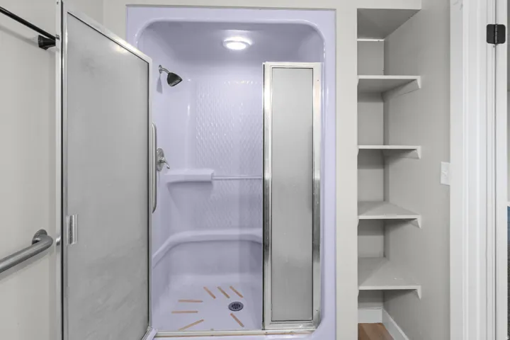 Enclosed shower with frosted glass door, integrated shower head, and built-in shelving